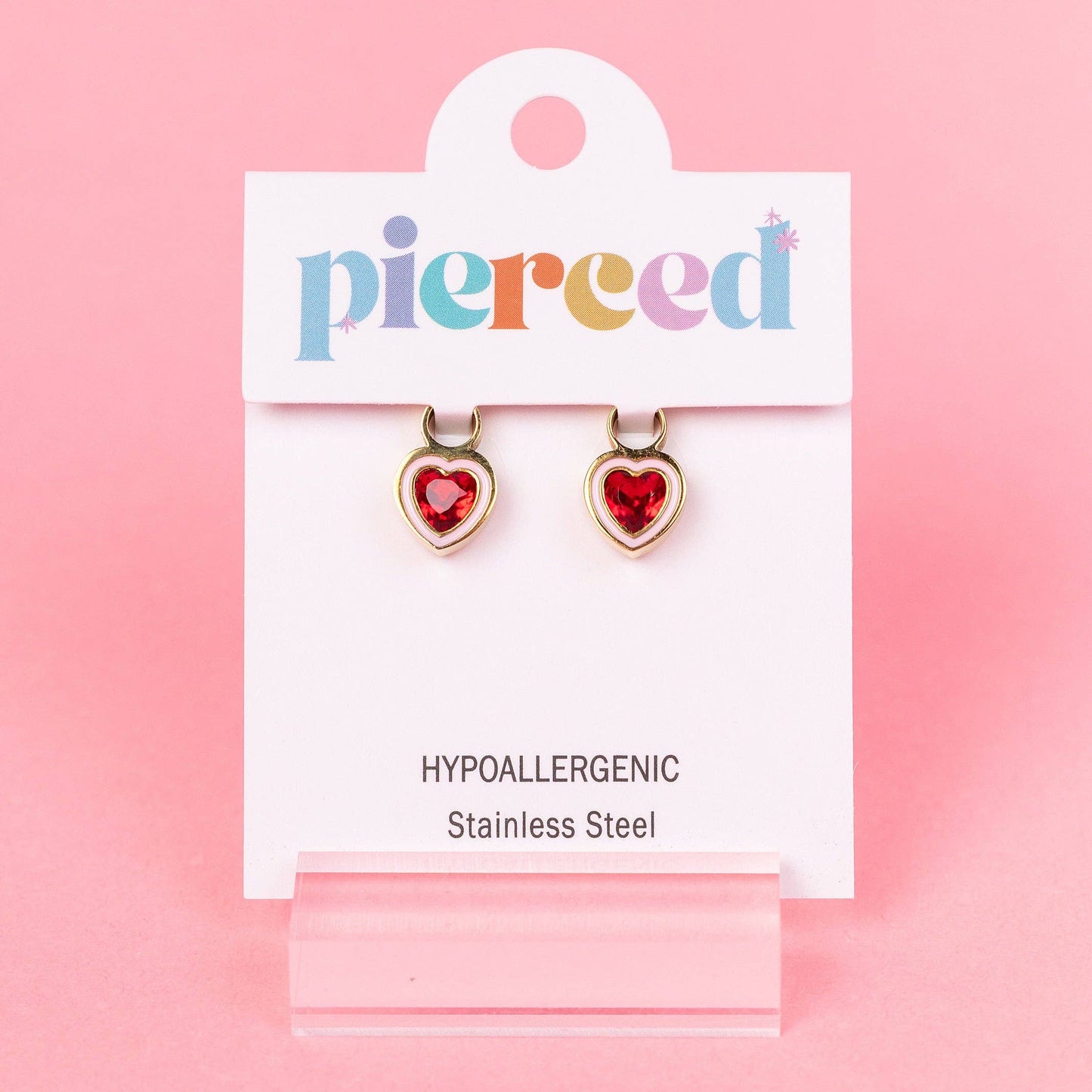 Heart-shaped earrings on a 'pierced' branded card against a pink background
