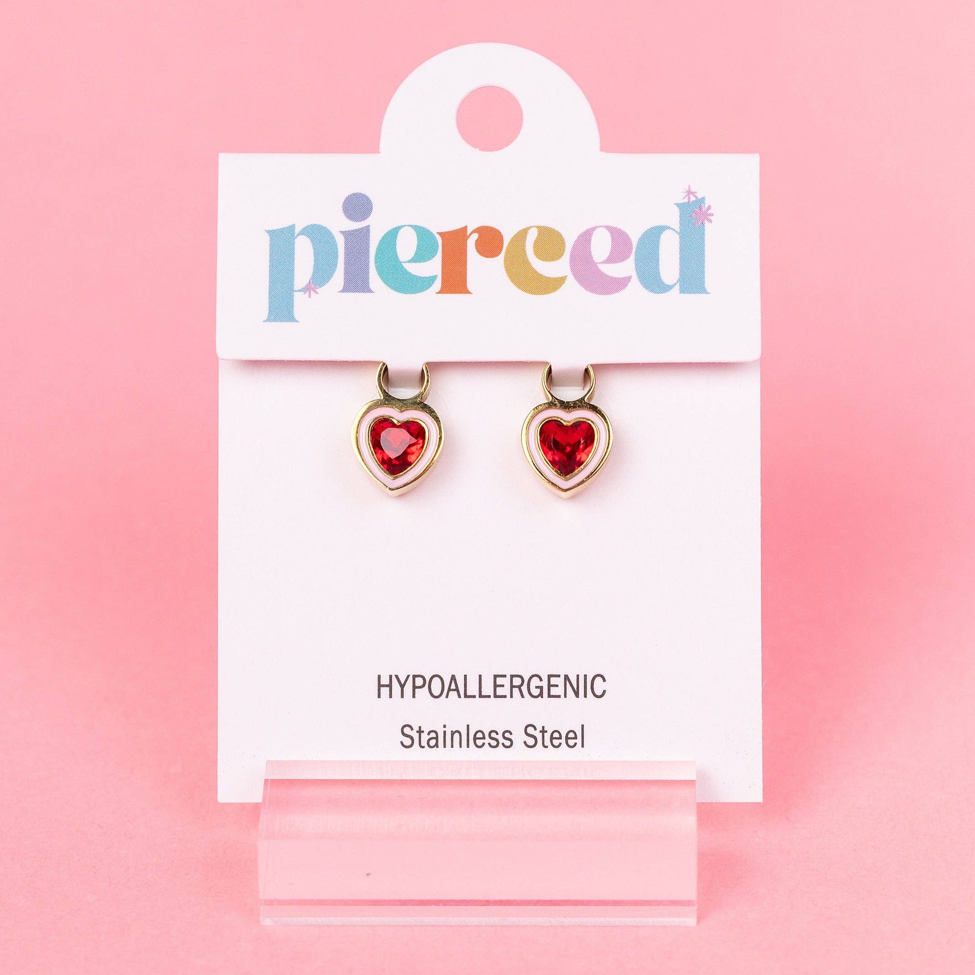 Heart-shaped earrings on a 'pierced' branded card against a pink background