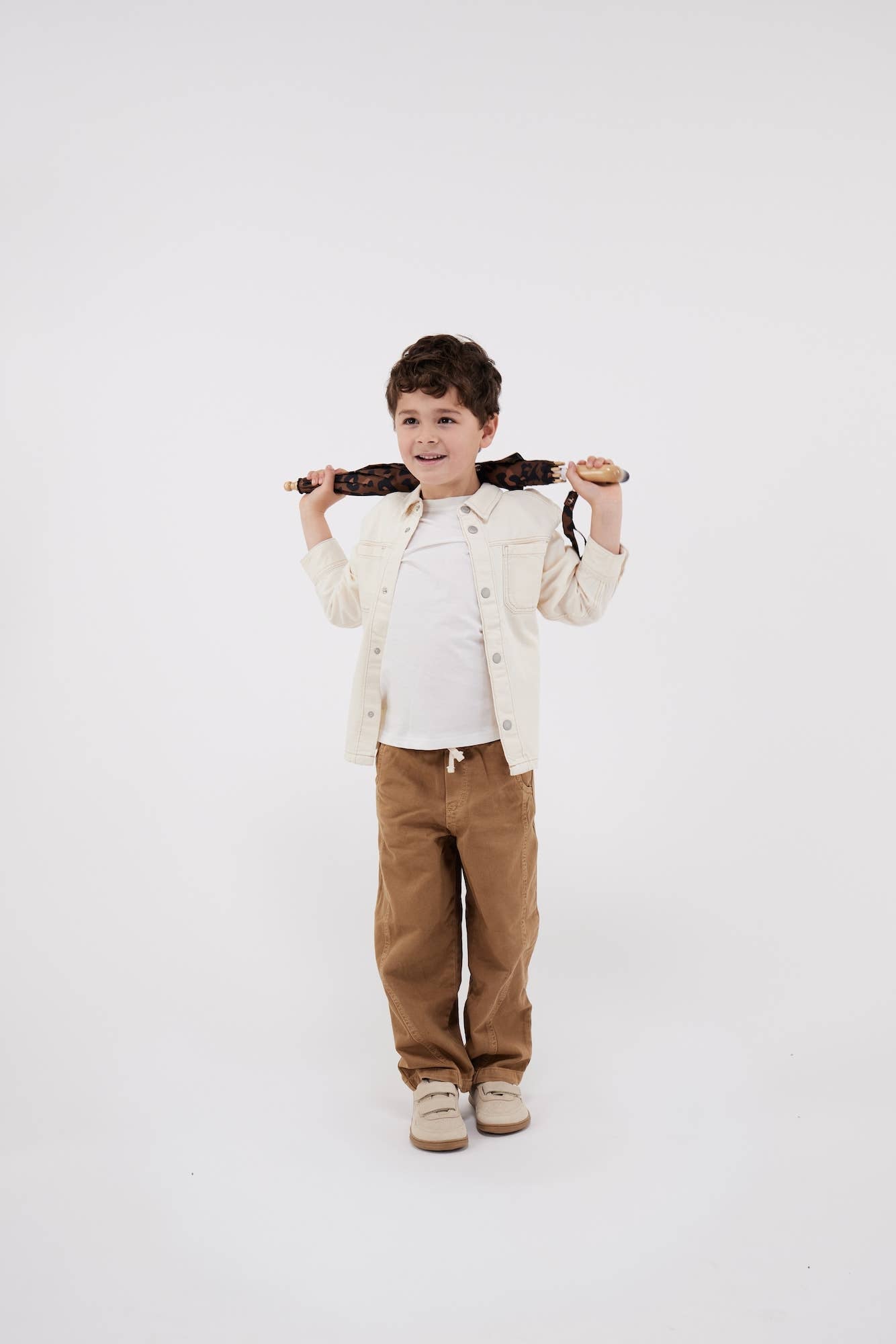 Child wearing a beige jacket and brown pants standing against a white background