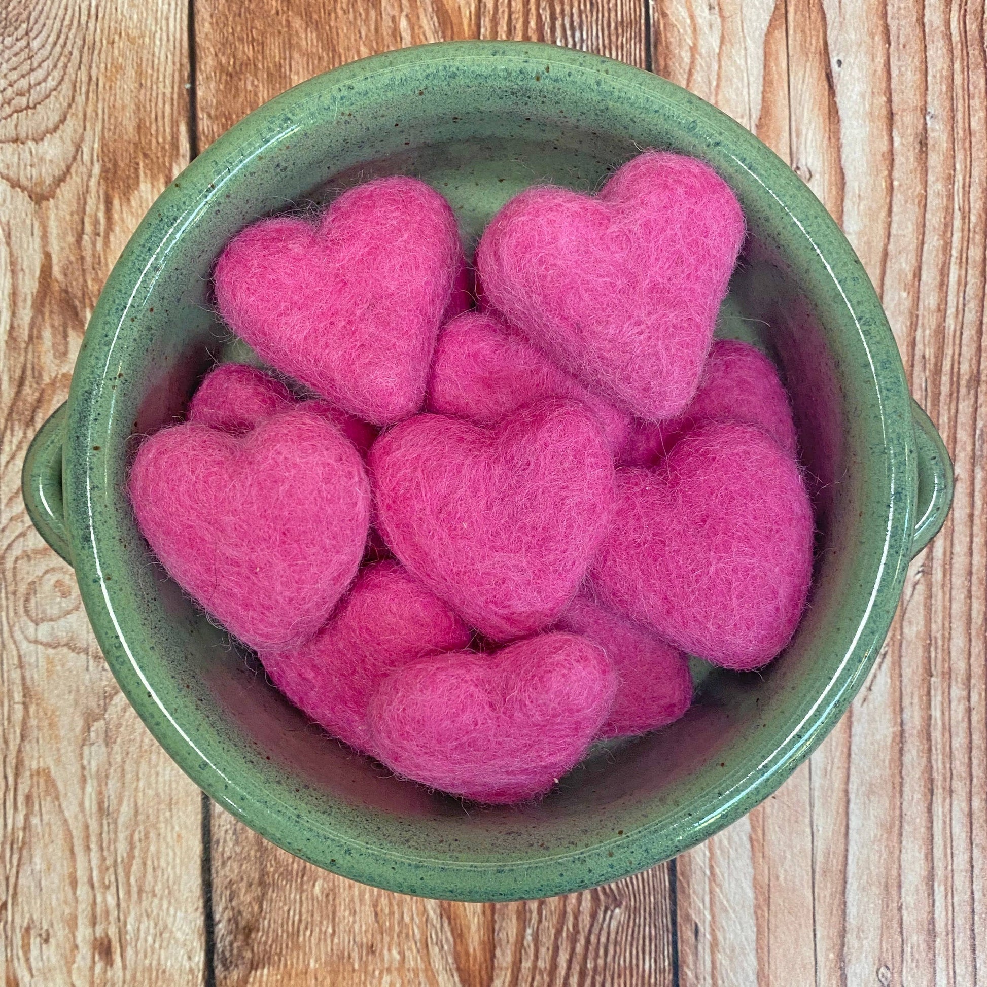 Green bowl filled with pink heart-shaped objects on a wooden surface