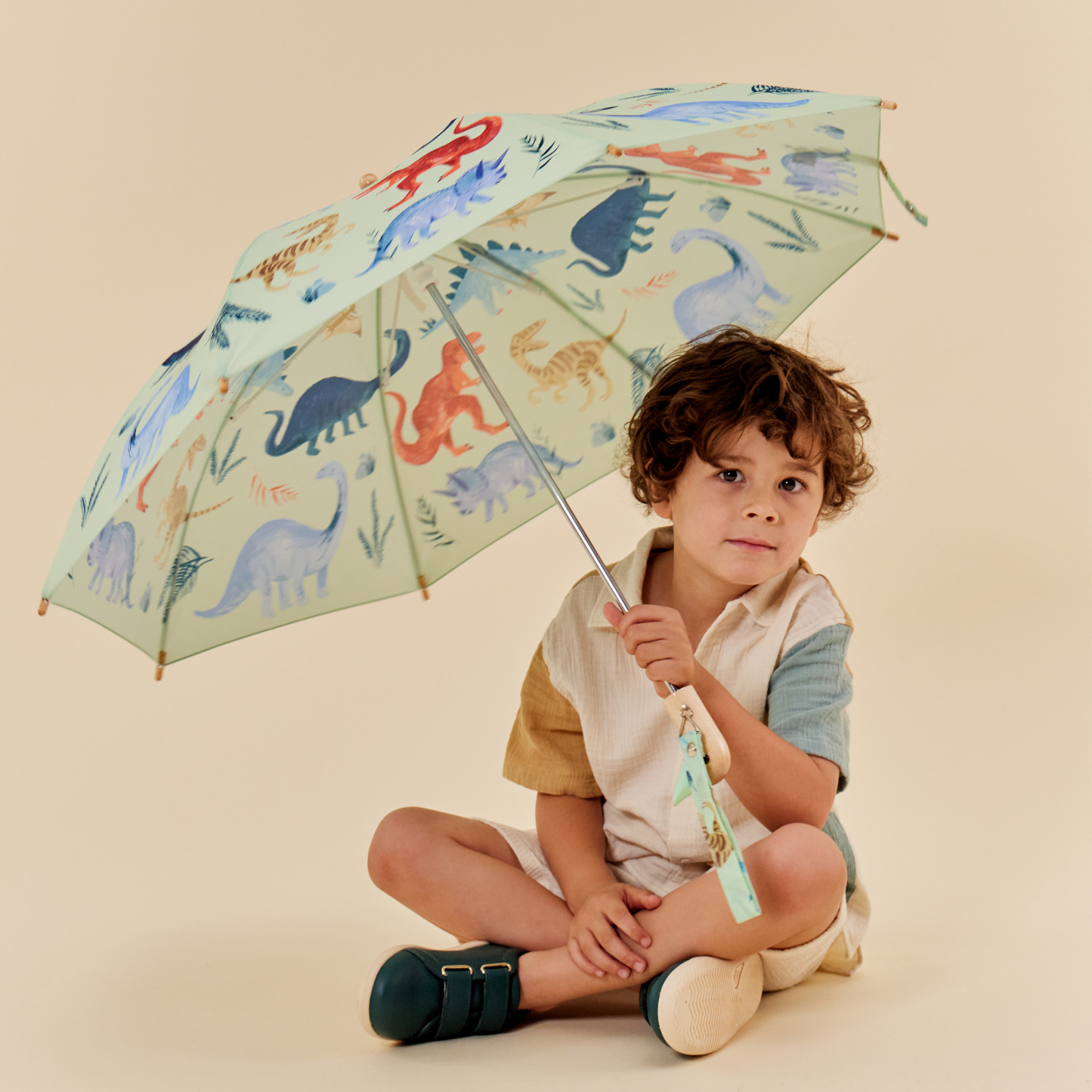 Child holding a colorful umbrella with dinosaur design on a beige background