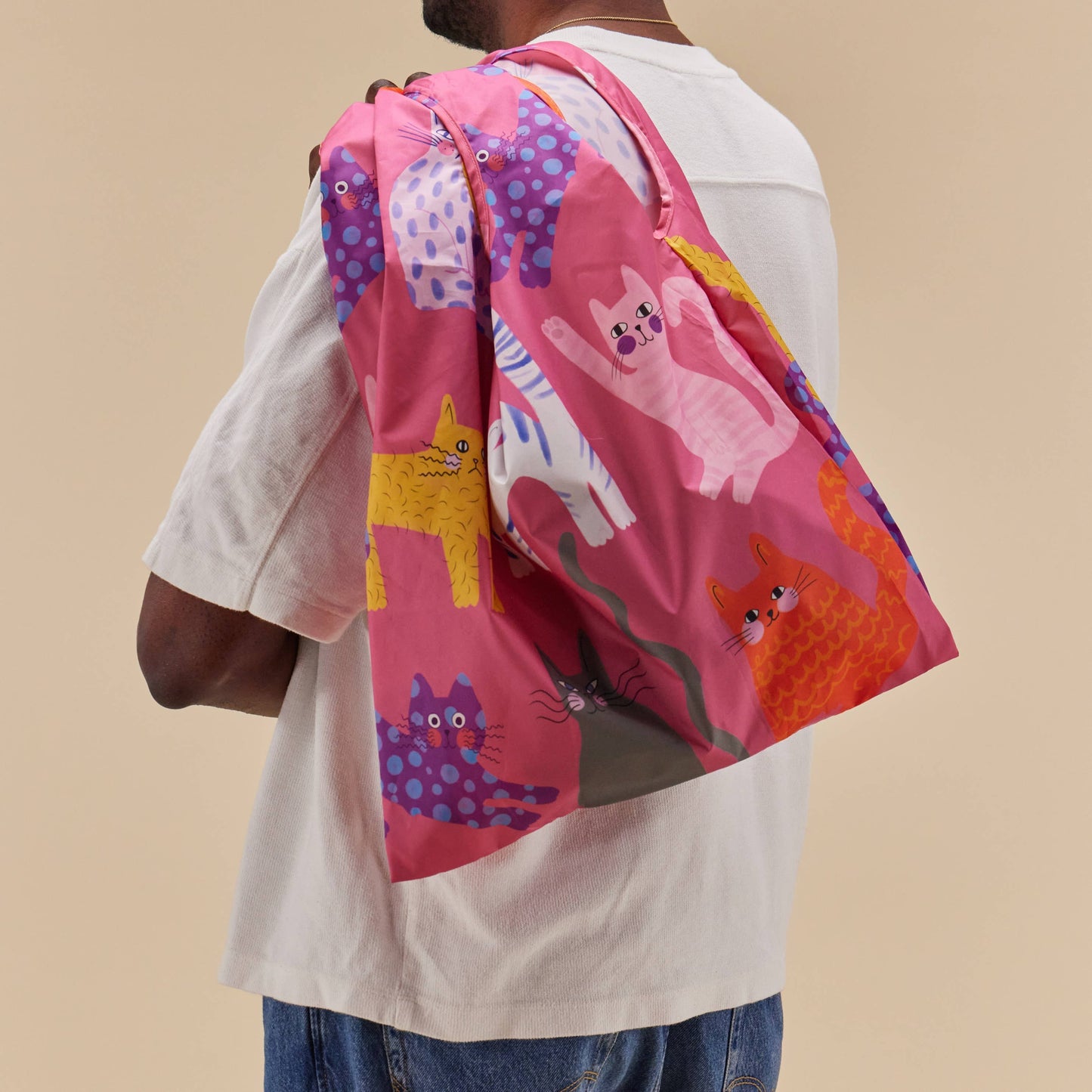 Person wearing a colorful pink tote bag with cat designs on a beige background
