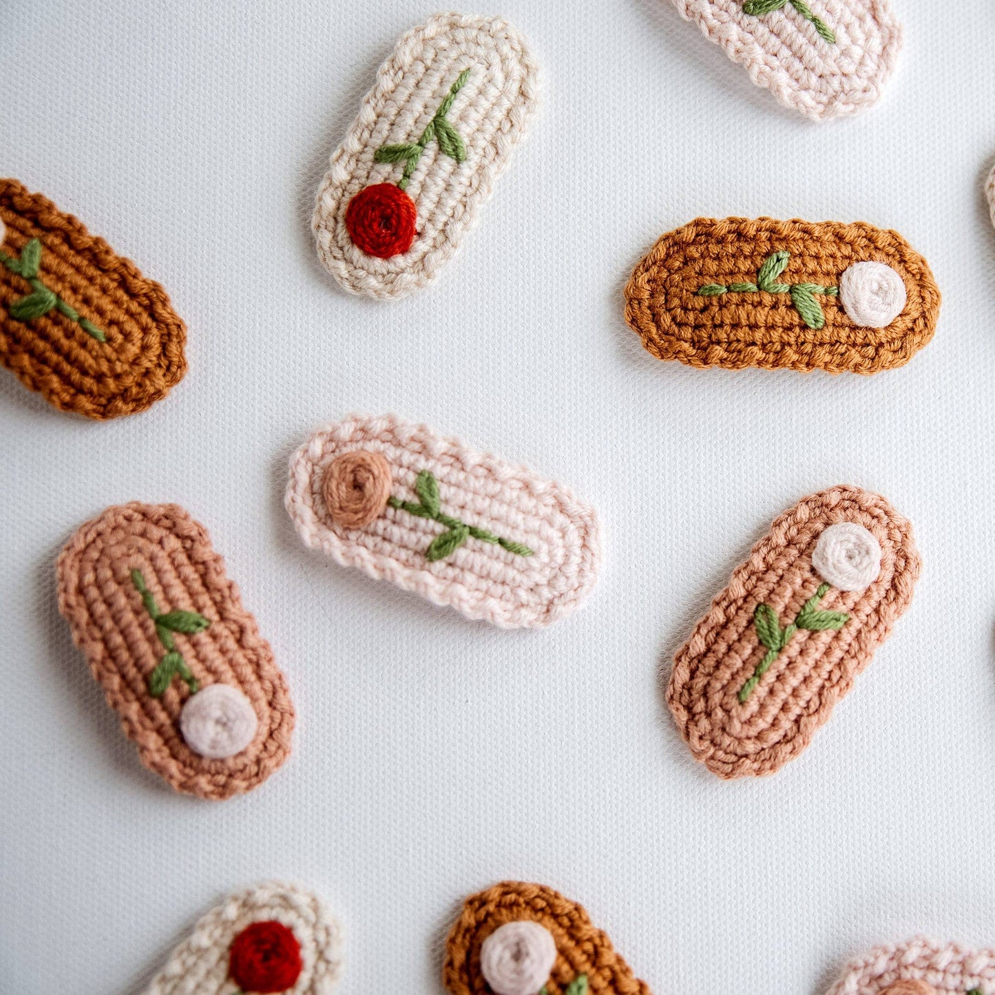 Pattern of crocheted pastries with floral decorations on a light background