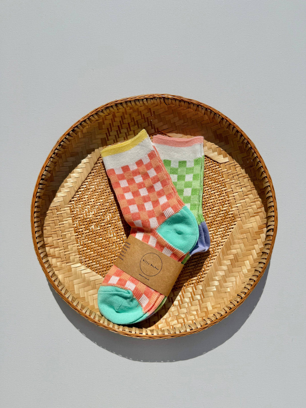 Colorful patterned socks displayed inside a round woven straw basket on a light gray background.