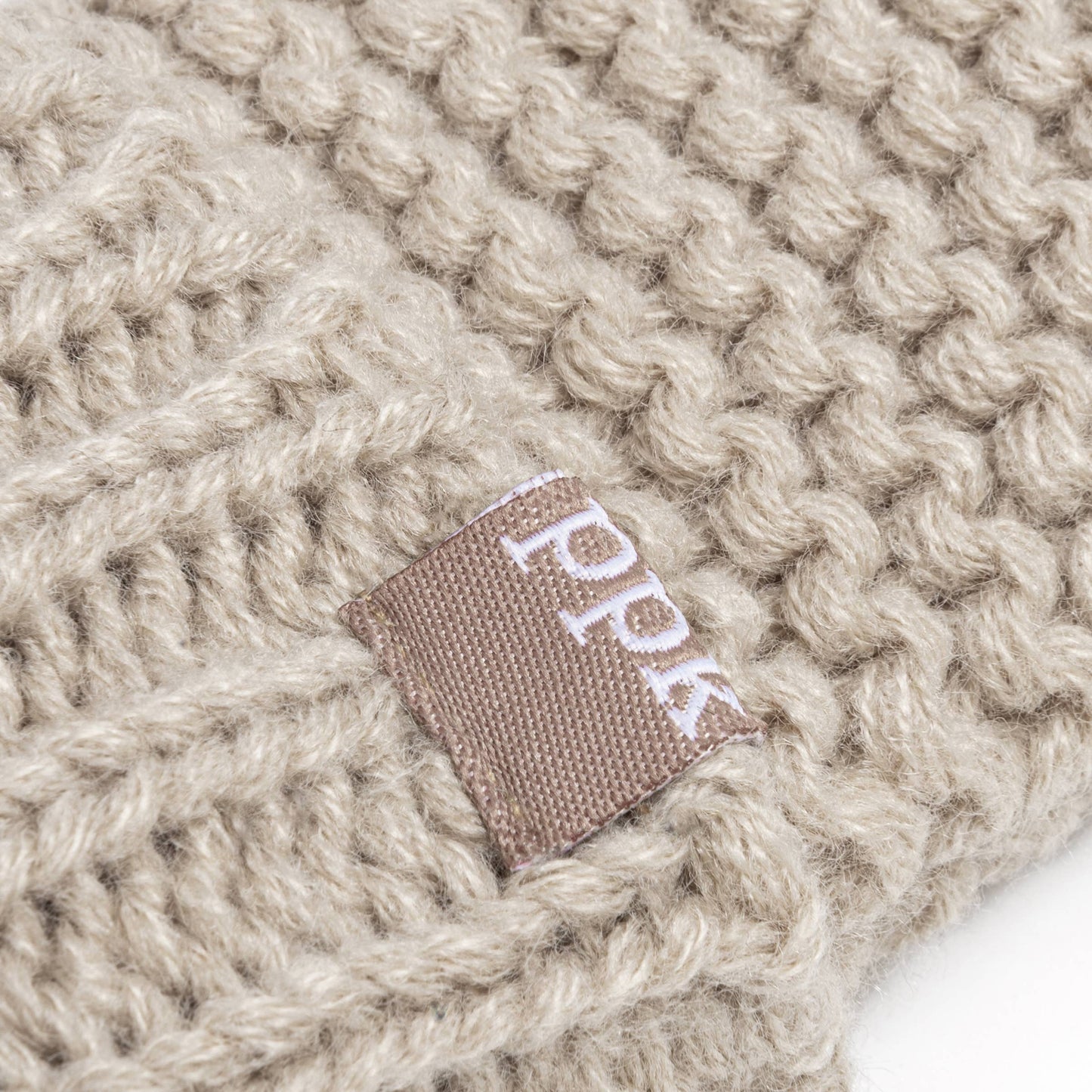 Close-up of a beige knitted fabric with a brand label on a white background