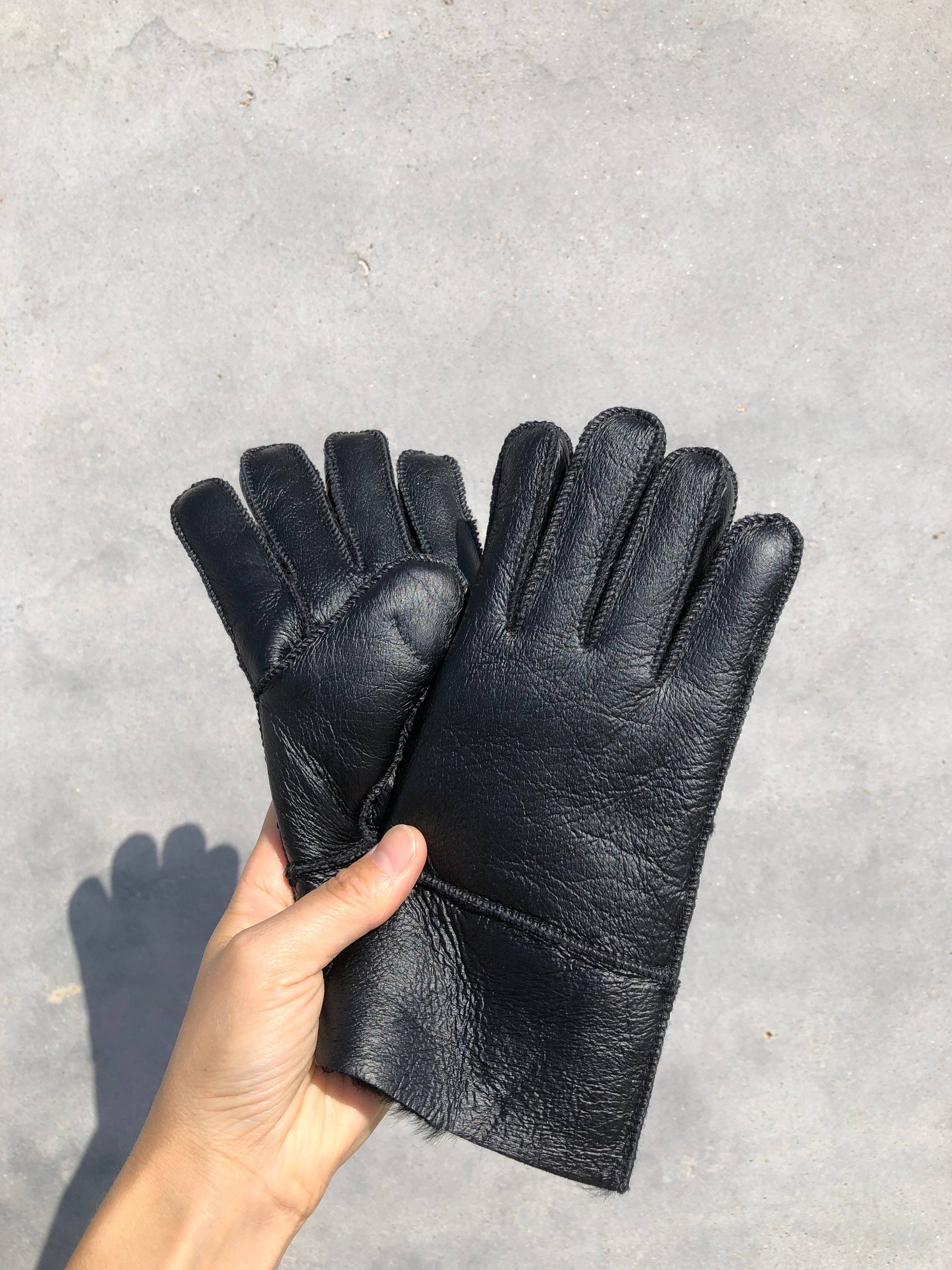 Black leather gloves held by a hand on a gray concrete surface