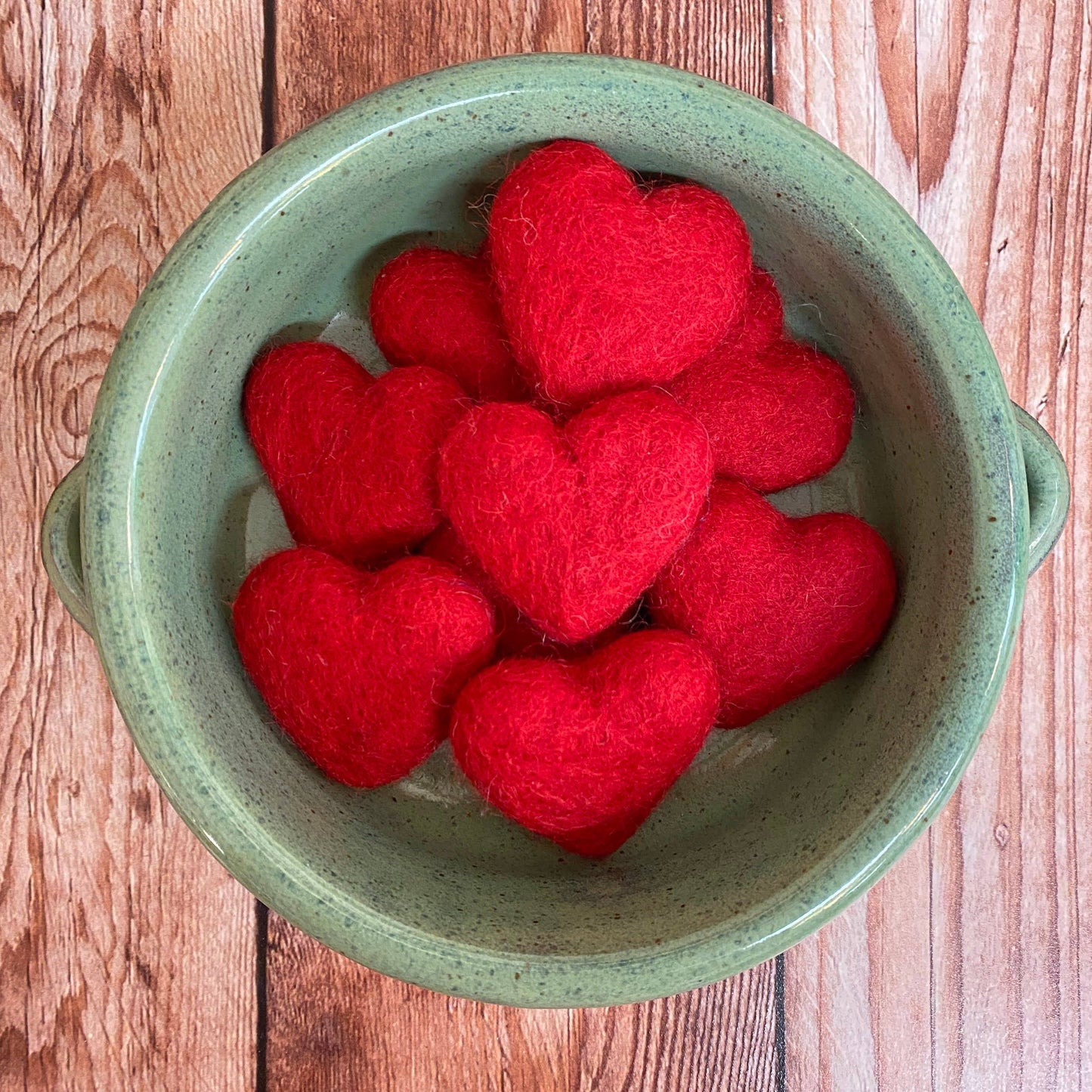 Red heart-shaped objects in a green bowl on a wooden surface