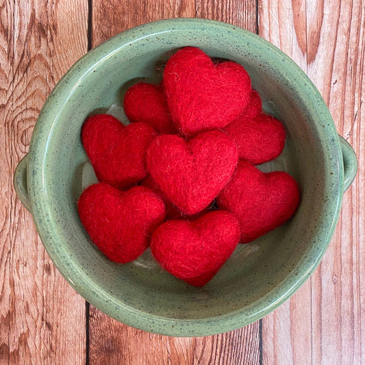 Red heart-shaped objects in a green bowl on a wooden surface