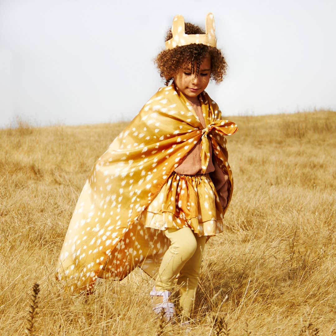Child in a deer costume standing in a field with a plain background