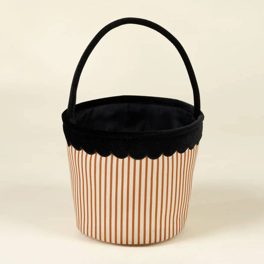 A small fabric storage basket with a black velvet handle and trim, featuring a white body with thin orange vertical stripes, set against a plain cream background.