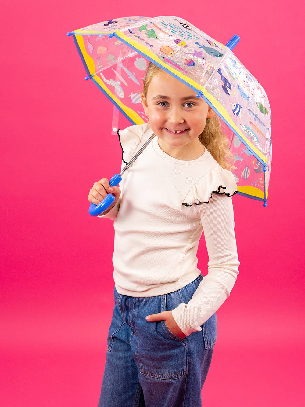 Young girl holding a transparent umbrella with colorful patterns against a pink background