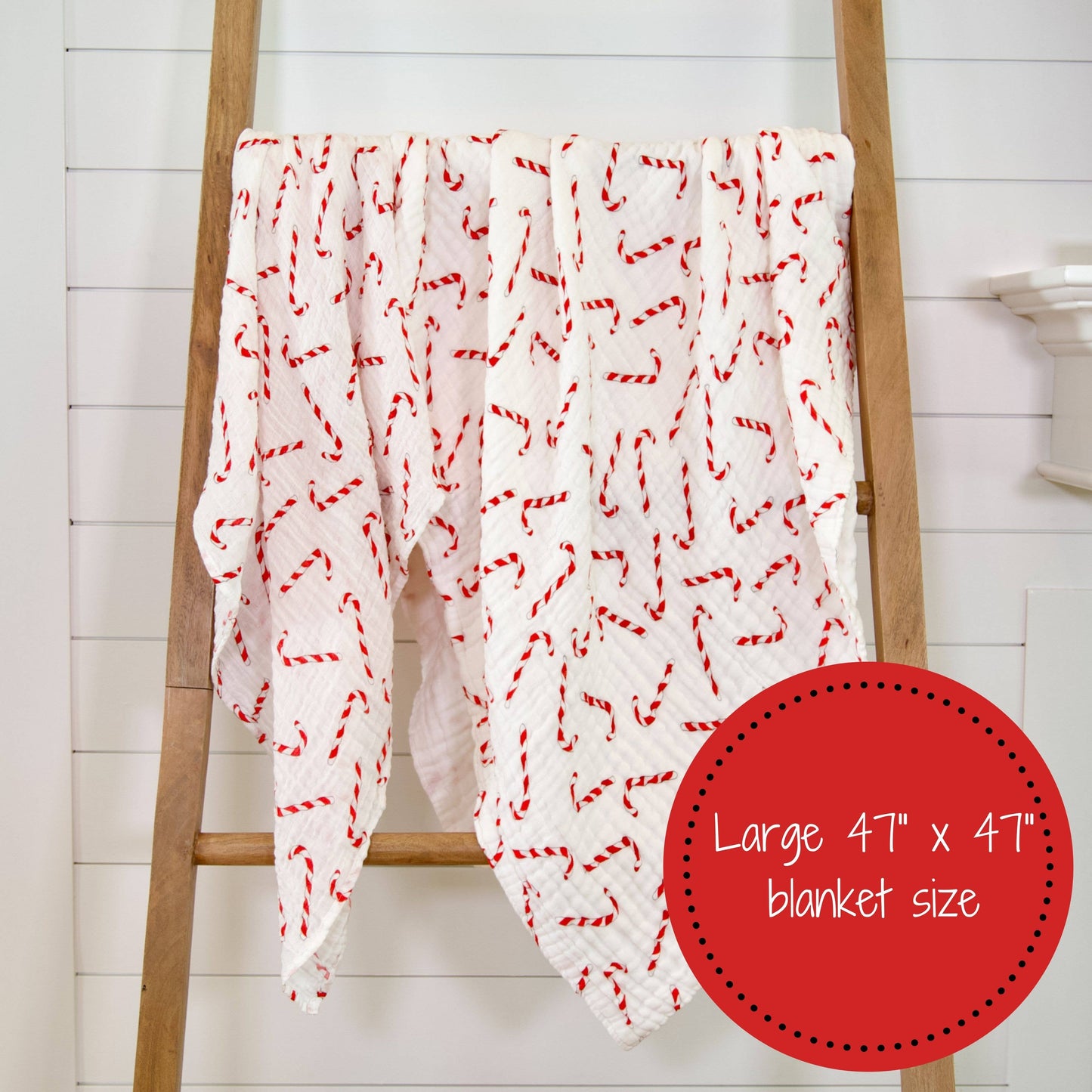 White blanket with red patterns draped over a wooden ladder against a white wall.