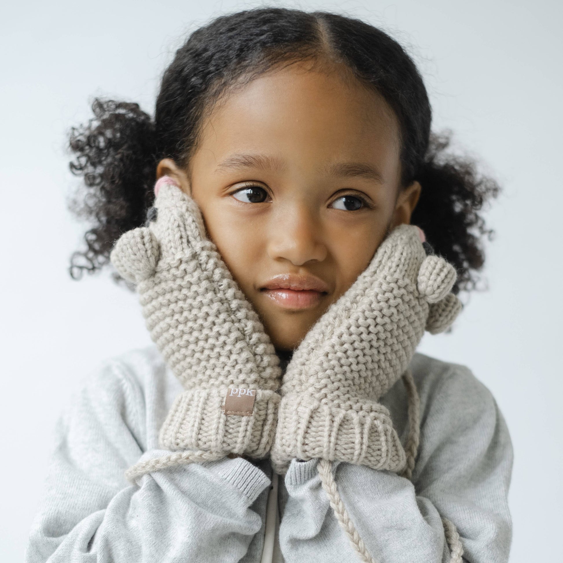 Child wearing beige knitted mittens against a light background
