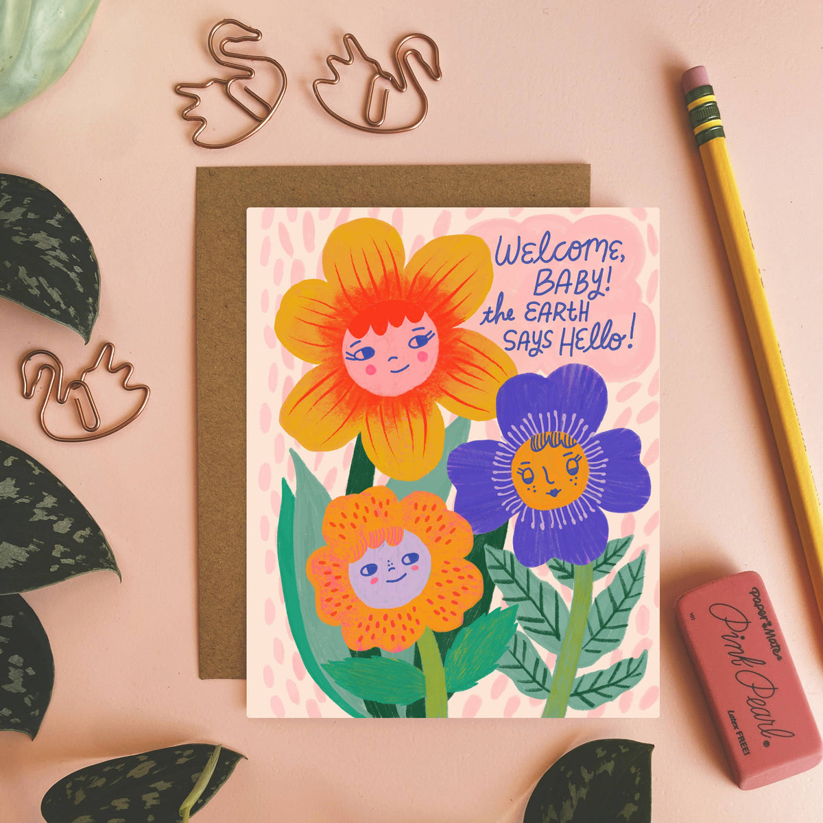 Greeting card with floral design and text on a pink background with stationery items.