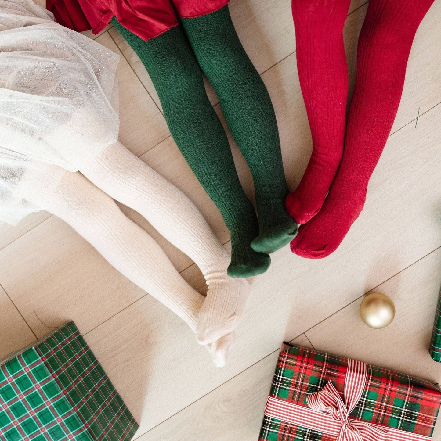 Two pairs of legs wearing green and red tights on a couch with Christmas presents.