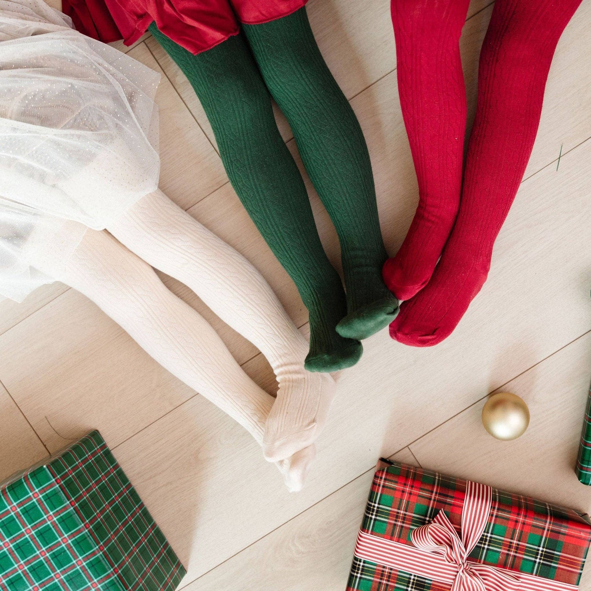 Two pairs of legs wearing green and red tights on a couch with Christmas presents.