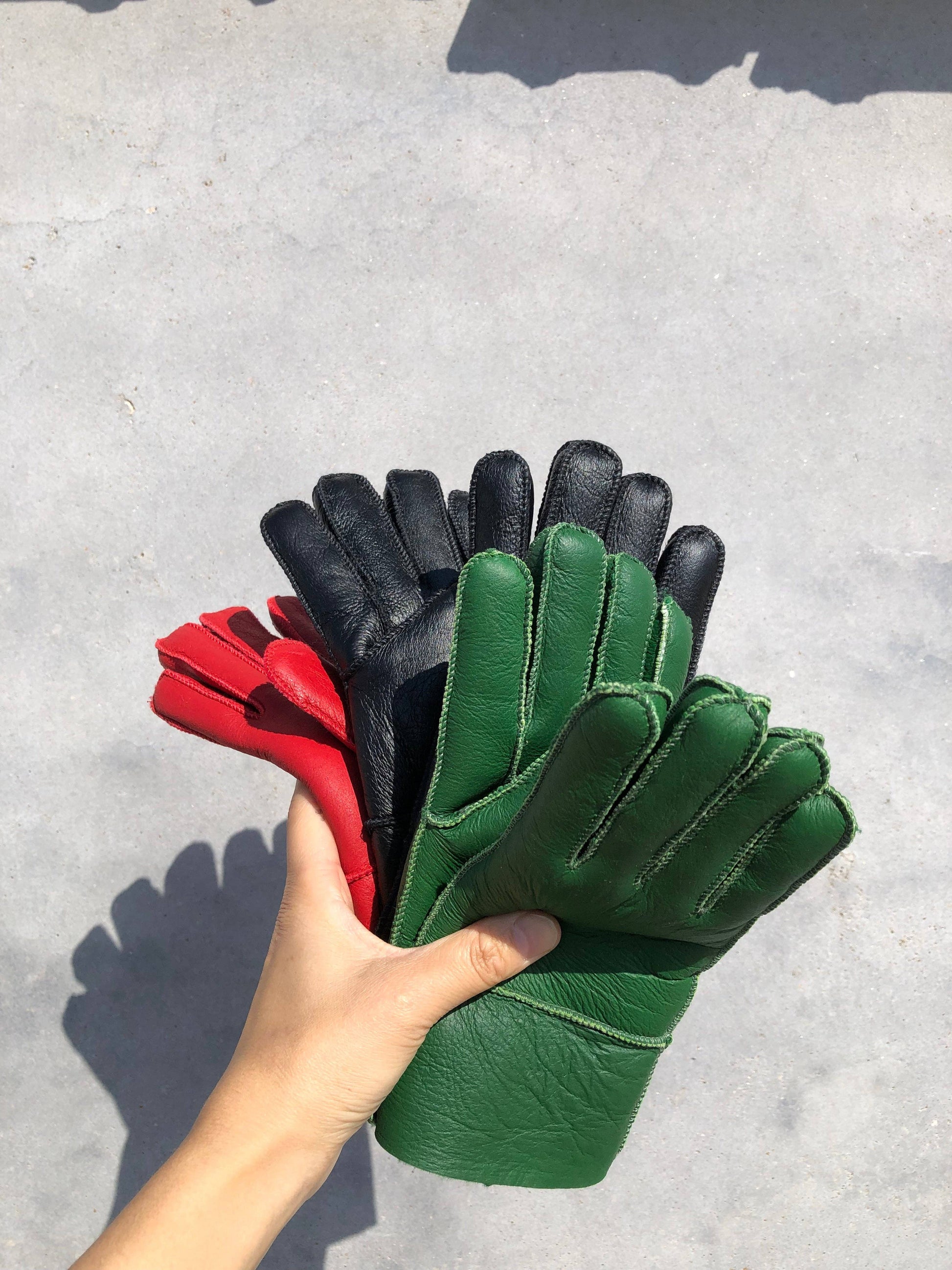 Hand holding a bundle of green, black, and red leather gloves on a gray surface.