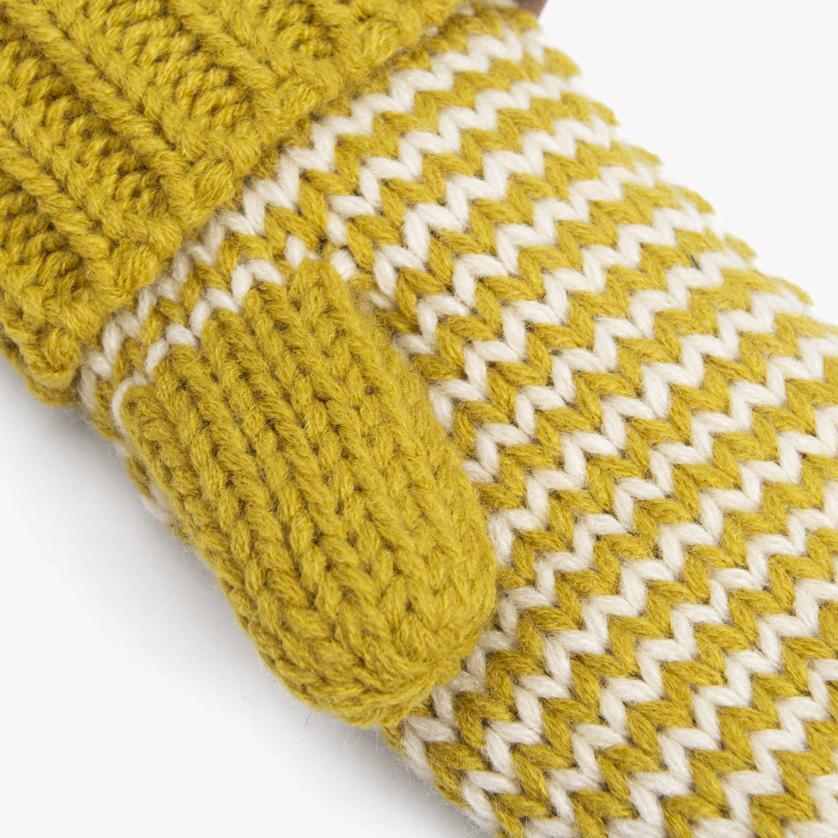 Close-up of a chunky knit winter glove in mustard yellow and white, showing the ribbed cuff and textured chevron pattern on a white background.