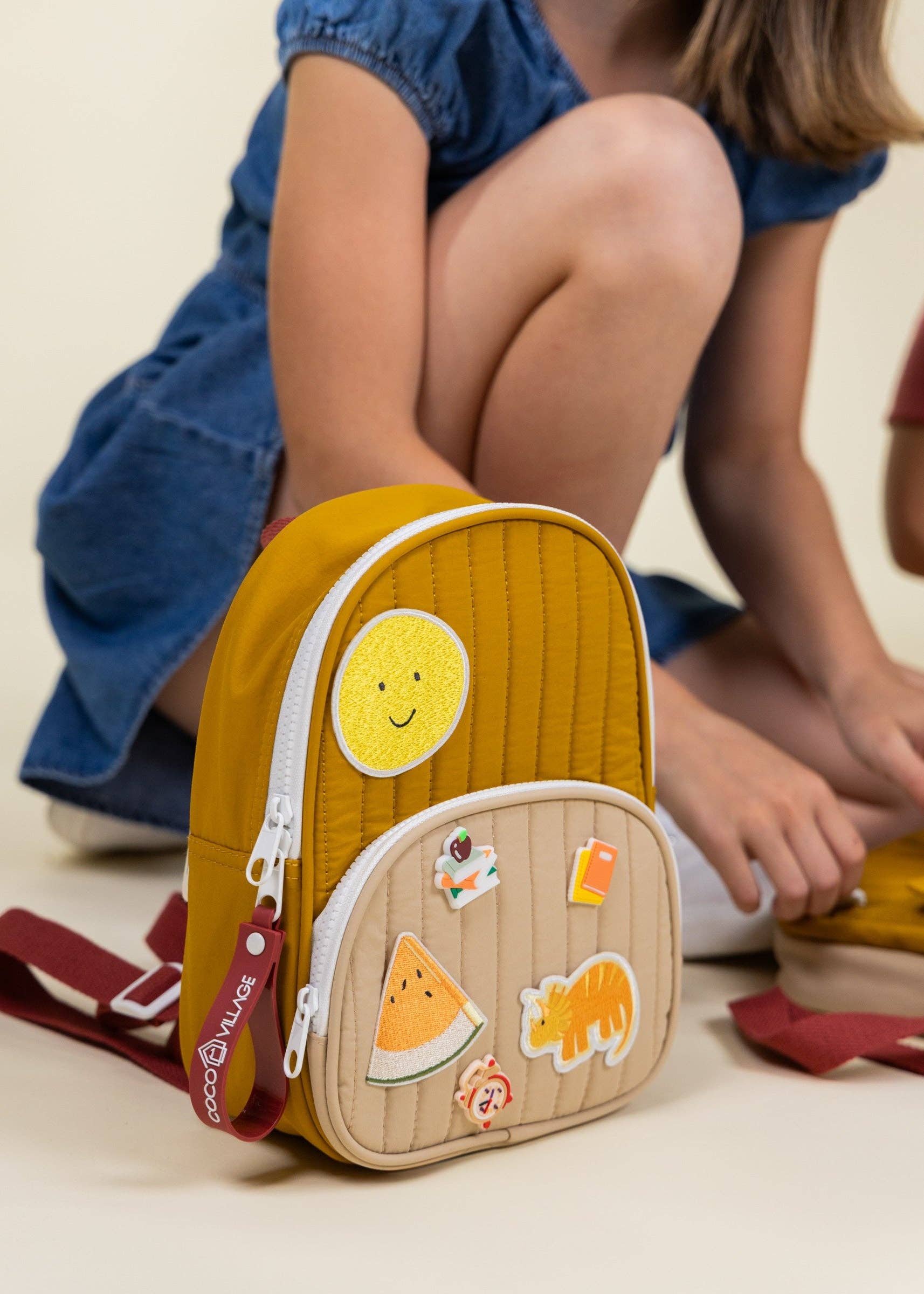 Children's backpack with a smiley face design and stickers, worn by a child in a blue dress.