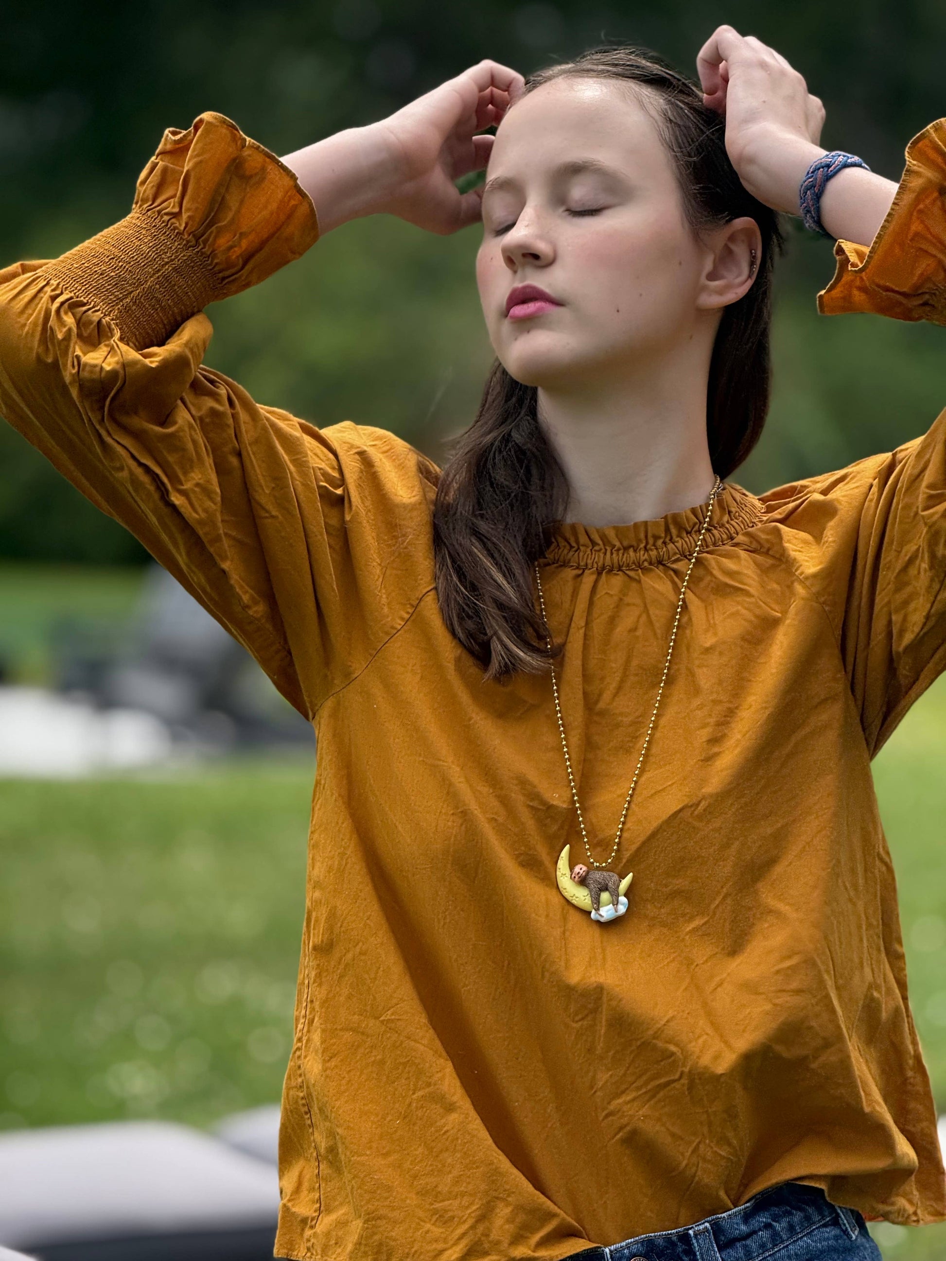 Woman in a mustard yellow shirt with her hands in her hair, standing outdoors.