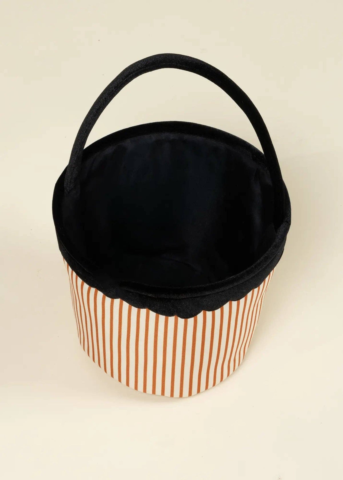 A fabric storage basket with a black handle and black interior, featuring a lower body with thin orange and white vertical stripes, set against a plain off-white background.