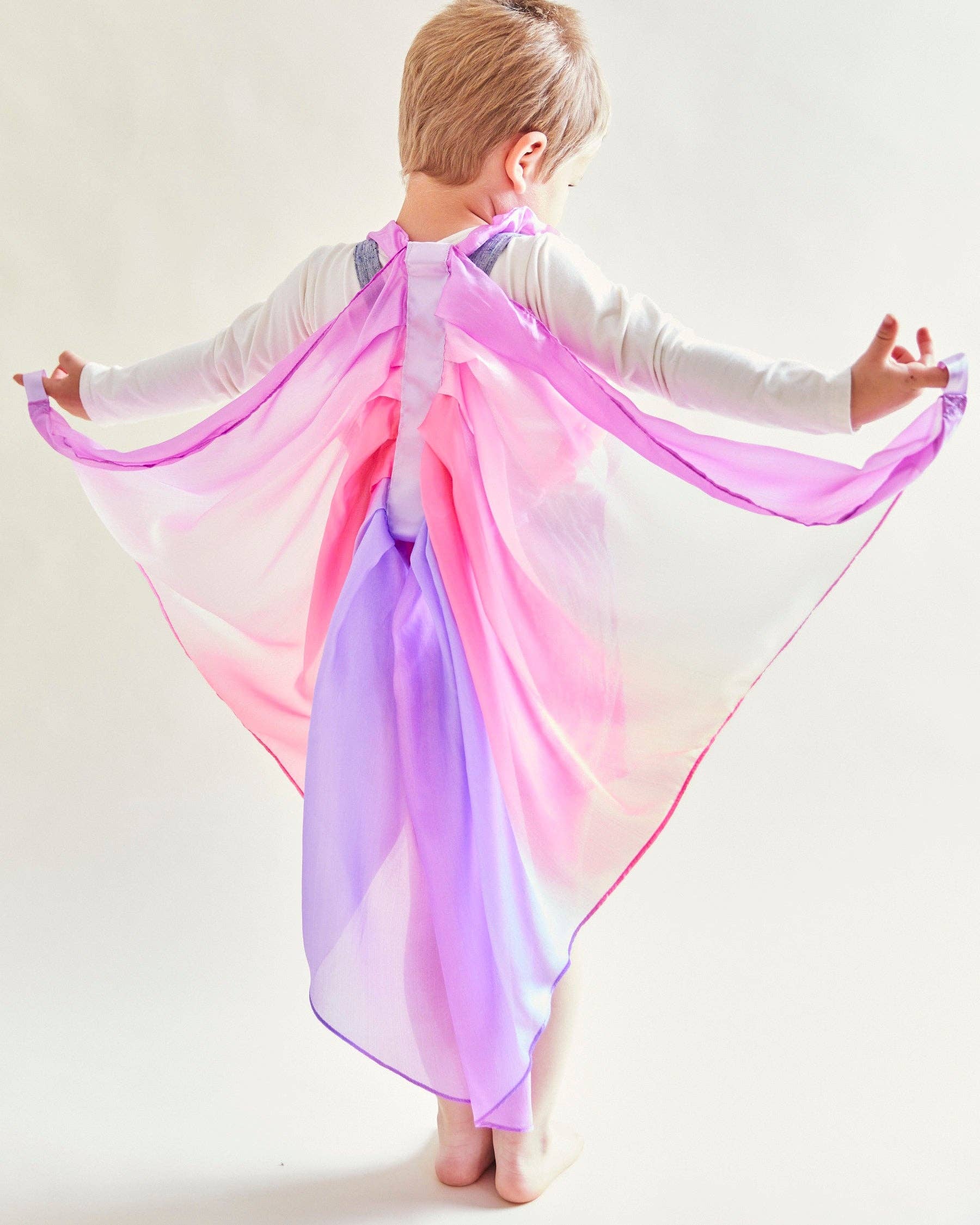 Child wearing a colorful cape with pink and purple gradient on a white background