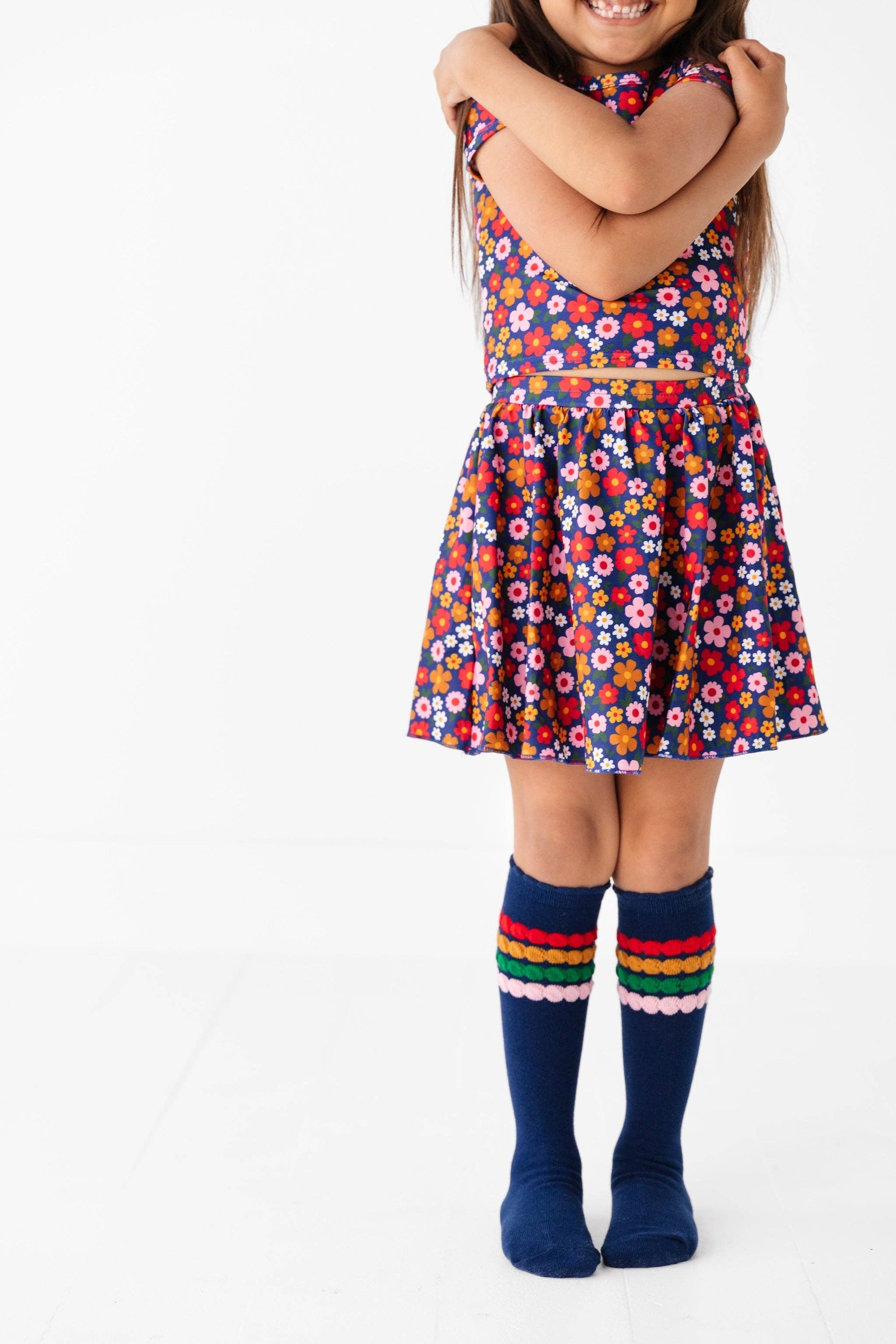 Child wearing a colorful floral dress with rainbow knee-high socks on a white background