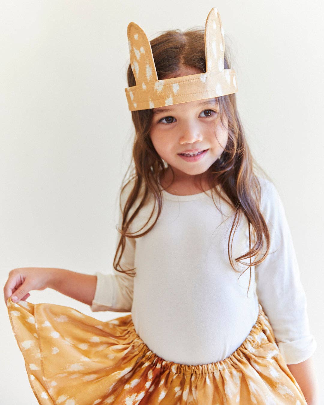 Child wearing a white top and yellow skirt with deer print, standing against a plain background.