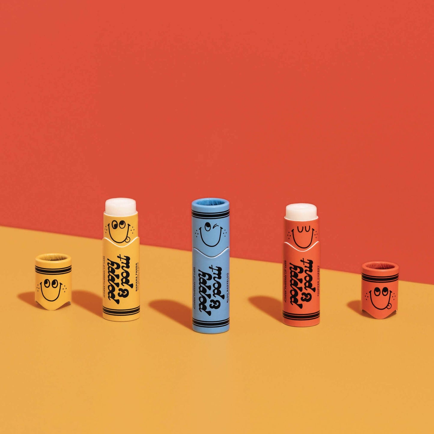 Set of colorful lip balm tubes with smiley face designs on a red and orange gradient background.