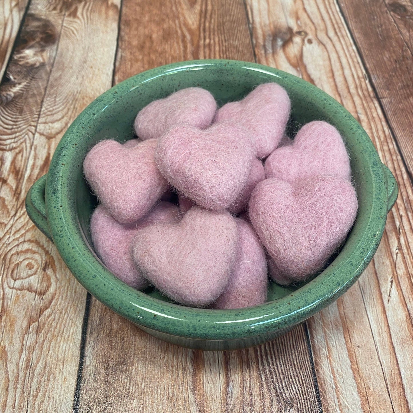 Pink heart-shaped objects in a green bowl on a wooden surface
