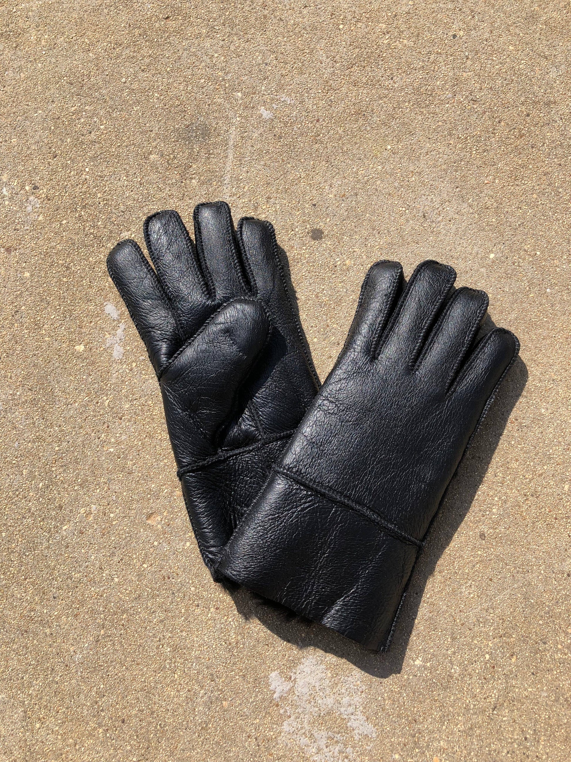 Pair of black leather gloves on a textured beige surface