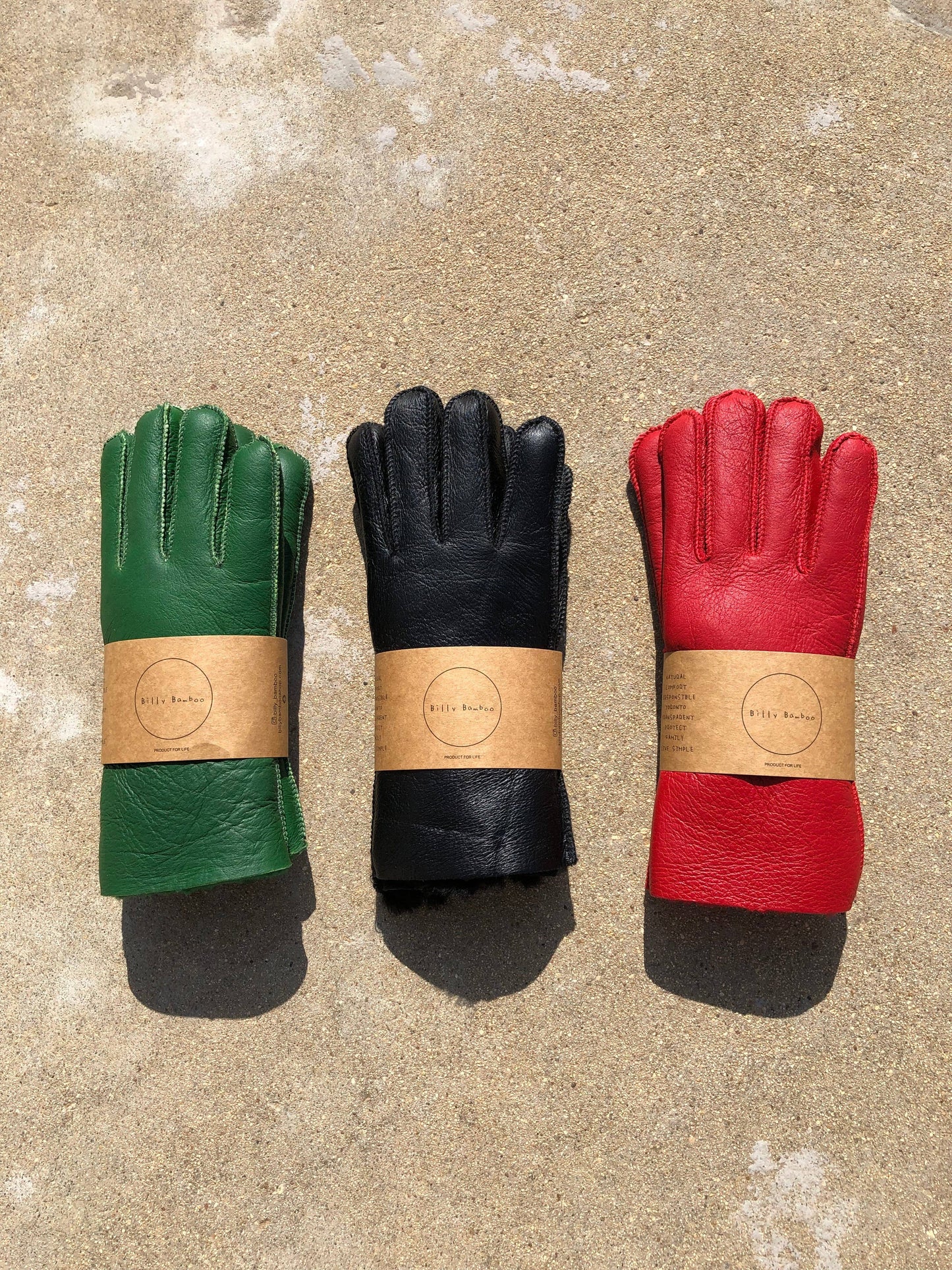 Three pairs of leather gloves in green, black, and red on a textured surface.