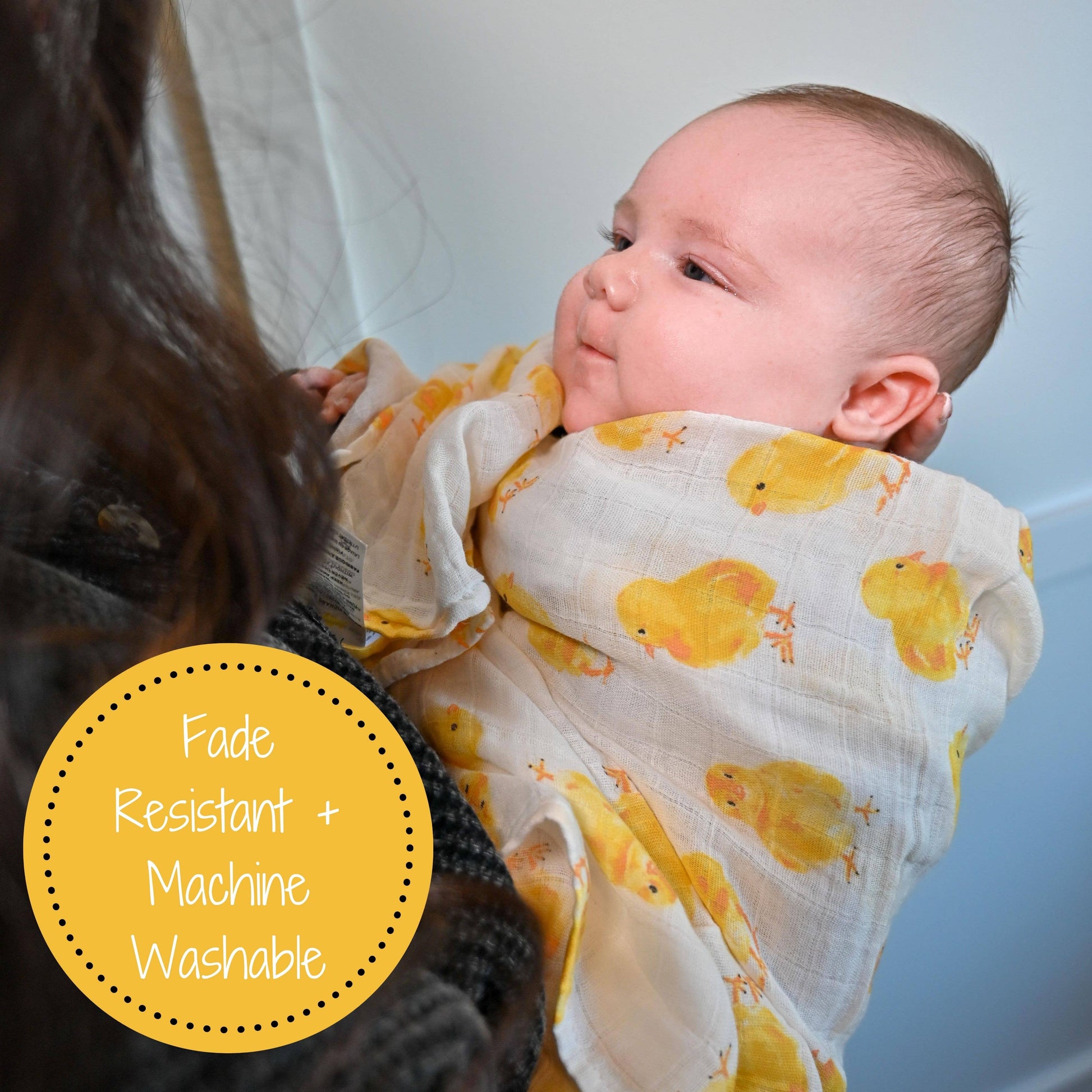 Baby wrapped in a yellow duck patterned blanket with text 'Fade Resistant + Machine Washable' on a light background.